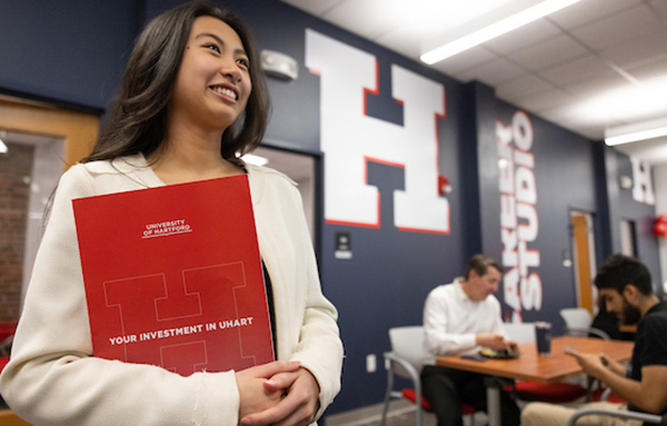 UHart student holds a red university folder, excited for the Sophomore Career Summit hosted by the Allan Center for Career and Professional Development.