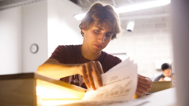 A male student flips through a stack of papers.