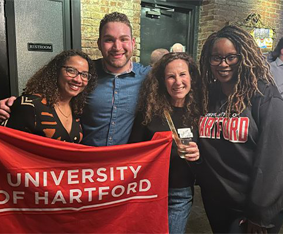 Three alumni holding a red UHart flag at a local Hawk Hangout.